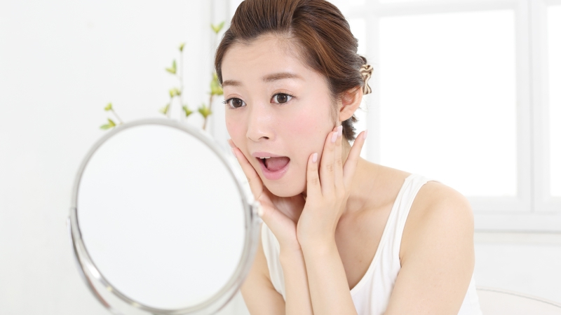 鏡を見ながら口を開く表情筋トレーニングをする女性