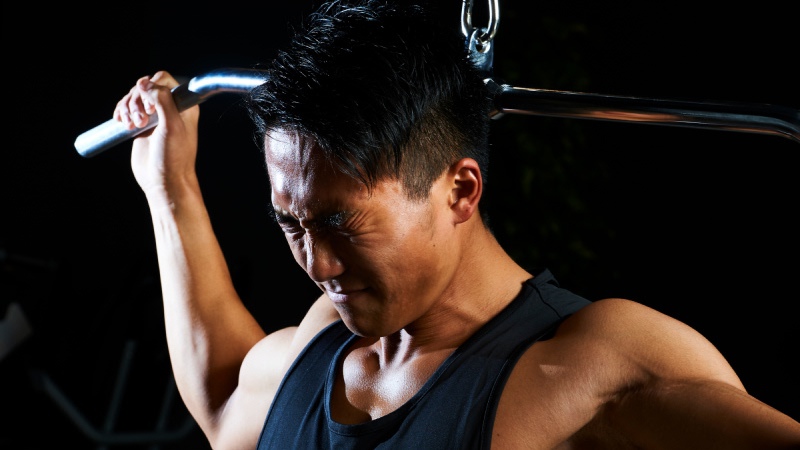 苦しそうな表情でラットプルダウンをする男性