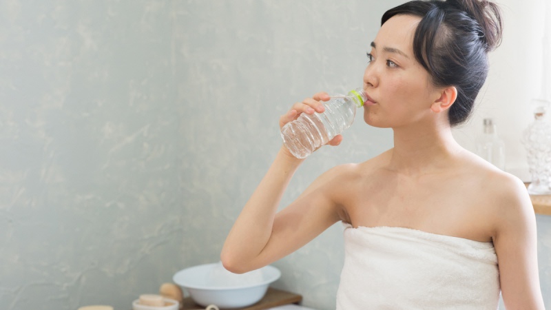 バスタオル姿で水を飲む女性